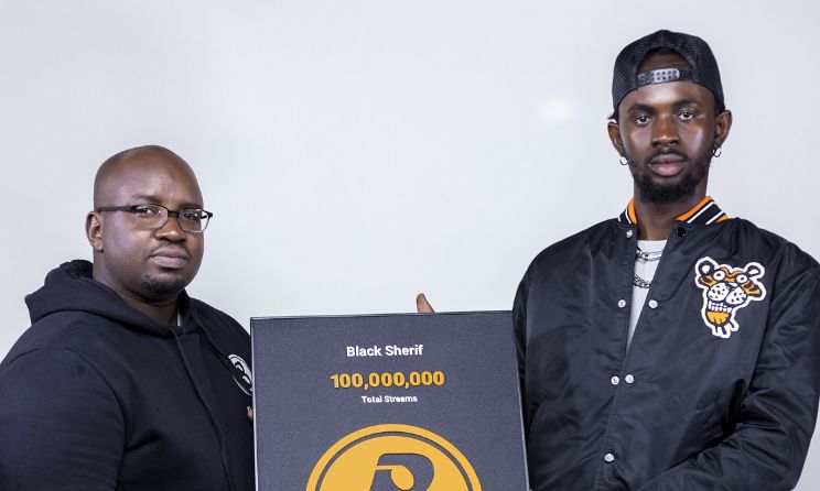 Boomplay Ghana public relations manager Paul Azumah-Ayitey presents Black Sherif with a plaque for surpassing 100 million streams on the platform.