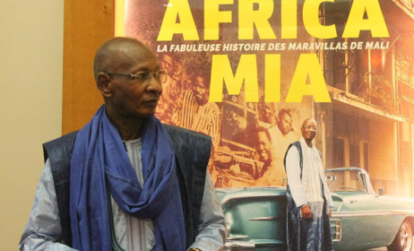 Boncana Maïga devant l'affiche d' « Africa Mia », projet cinématographique retraçant le parcours exceptionnel du groupe Las Maravillas du Mali (Photo) : gnakrylive.com